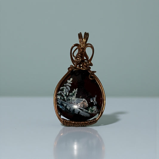 Bronze pendant with a scenic design on a light gray background